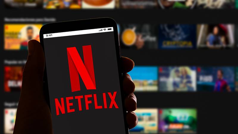 In this photo illustration the streaming app Netflix logo is seen on the screen of a mobile phone with the website homepage in the background.